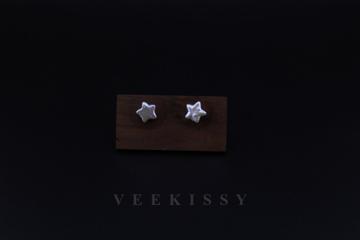 A pair of handcrafted star-shaped baroque pearl earrings displayed on a wooden stand against a black background, featuring natural freshwater pearls set on sterling silver studs.