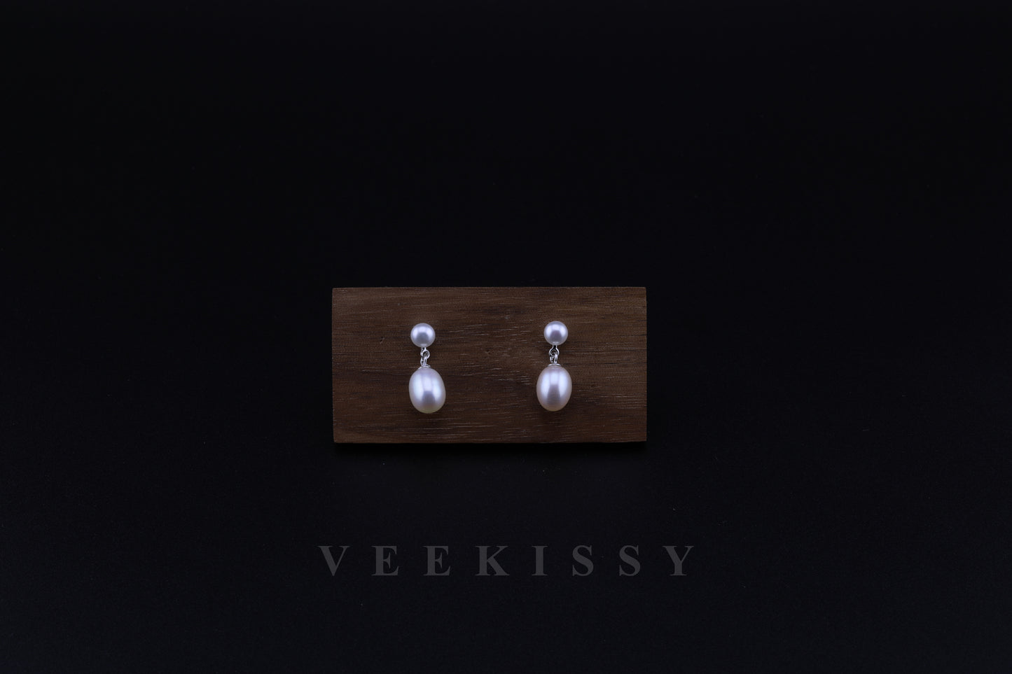 A pair of double freshwater pearl drop earrings, featuring a round stud pearl and an oval drop pearl, set on 925 sterling silver, displayed against a black background with a wooden stand.