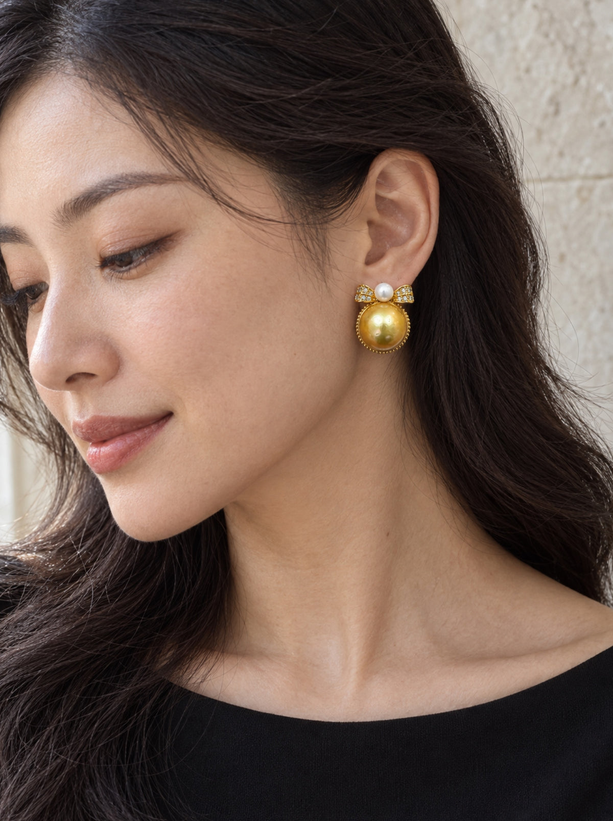Golden bow pearl earring worn with a black neckline and swept-back hair