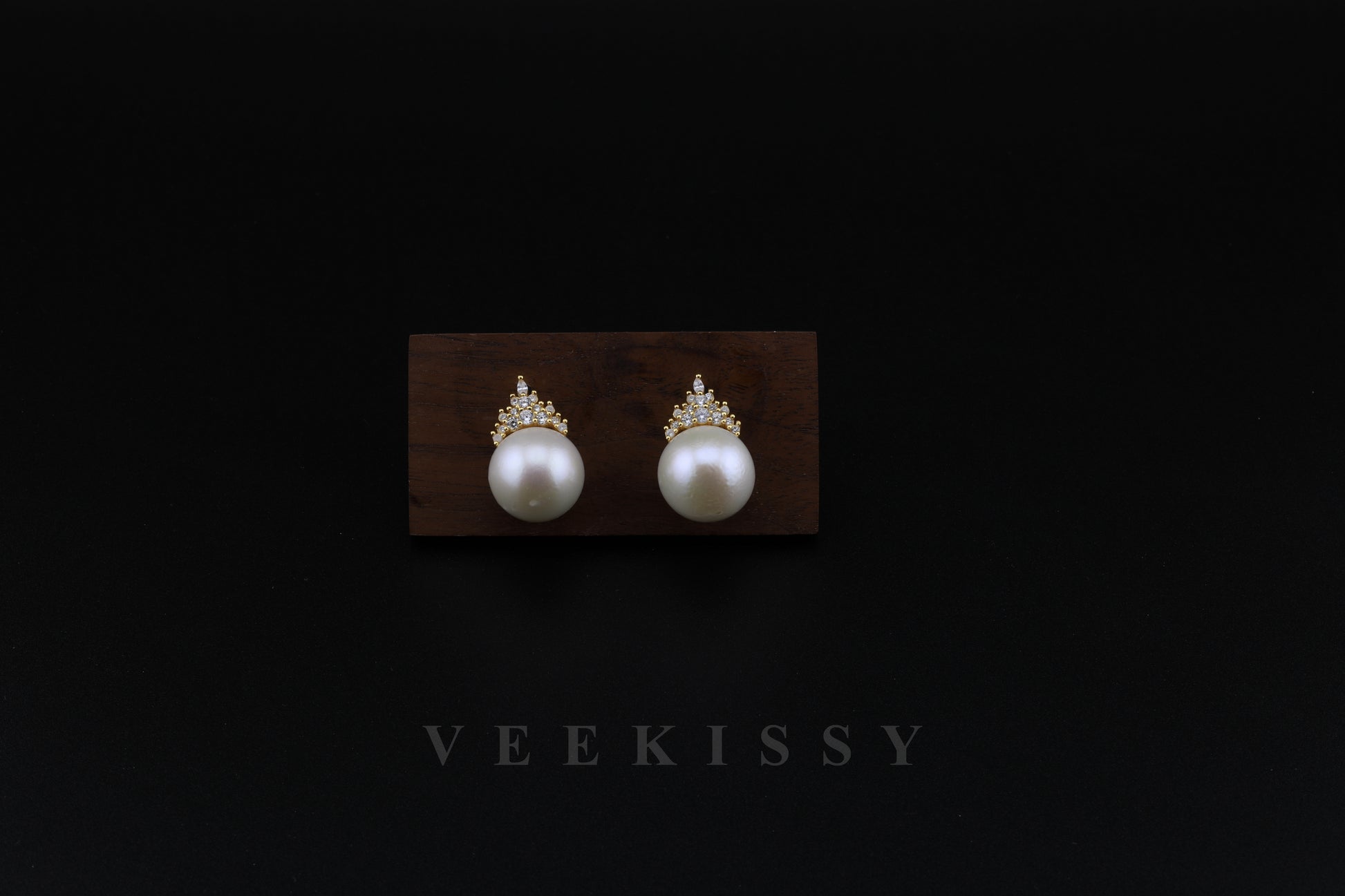 A pair of elegant freshwater pearl stud earrings with gold-plated sterling silver and delicate crystal accents, displayed on a wooden stand against a black background. Perfect for weddings, special occasions, and everyday luxury.