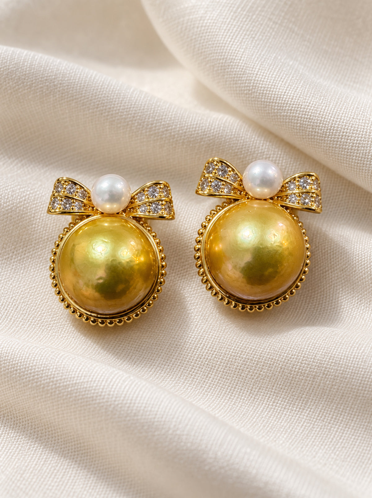 Pair of golden and white pearl bow earrings resting on ivory linen