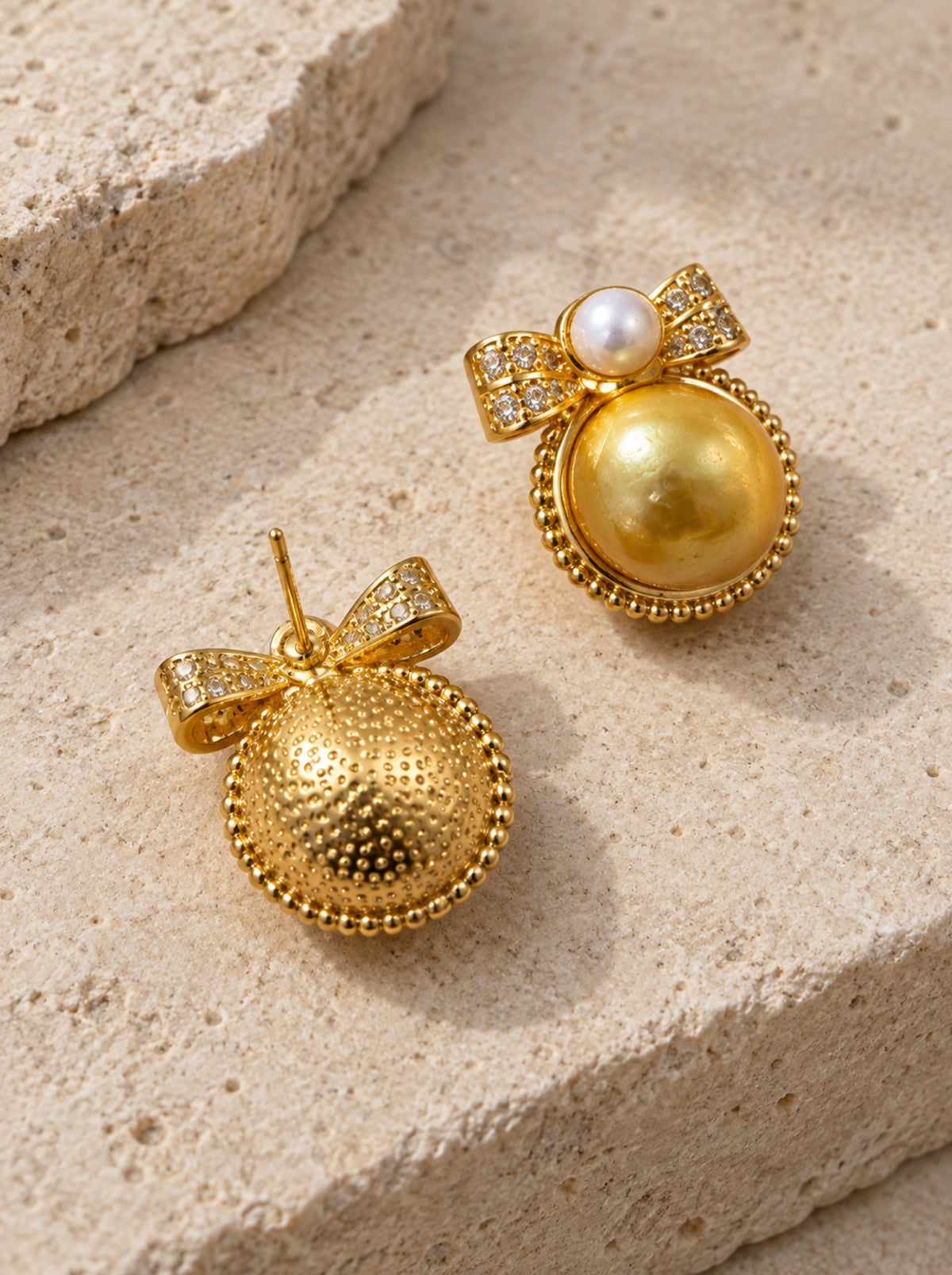 Reverse stud post and side view of golden bow pearl earrings on pale stone